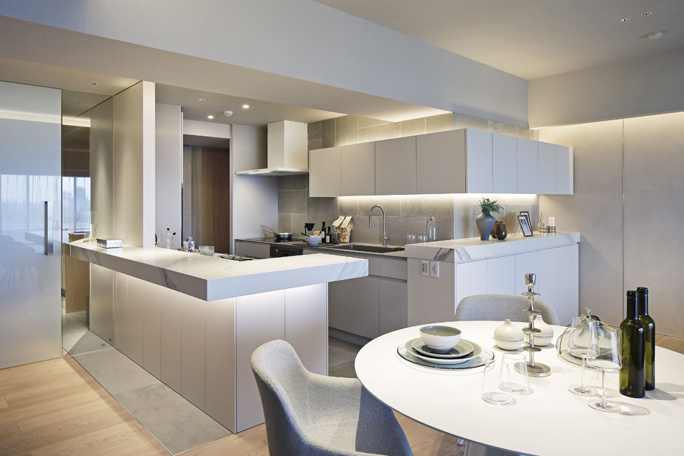 玄関ホールから延長されたL型カウンターと一体化するキッチン　背面の吊戸もL型