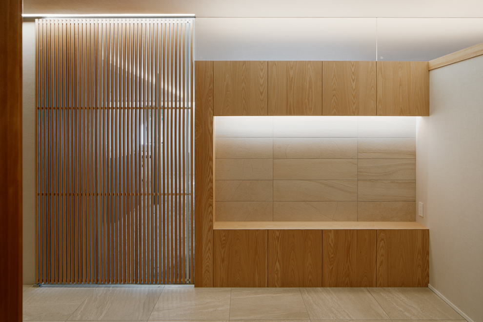 玄関ホールから飾棚とリビングへのルーバー扉をみる。飾棚の上部は透明ガラスを設置